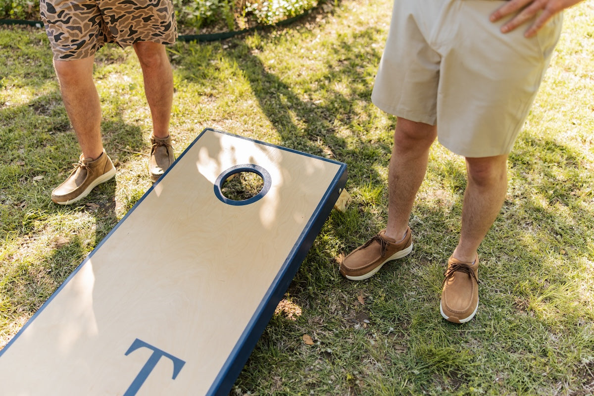 Two men wearing Feather X standing next to corn hole board